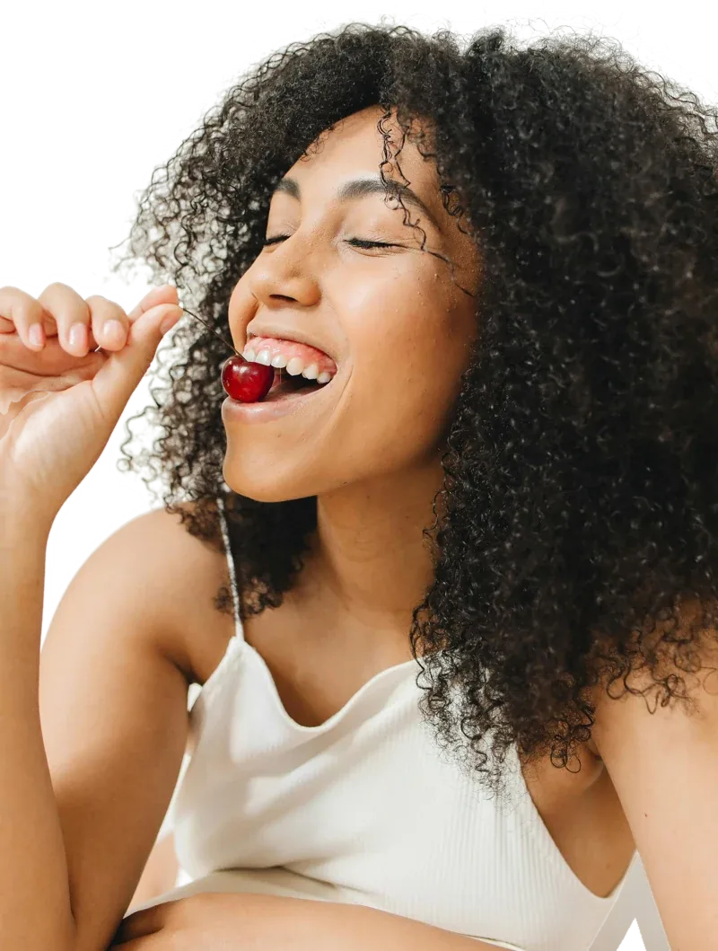 A person laughing as they bite into a cherry
